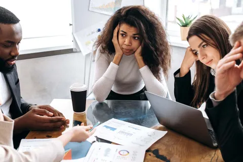 Mitarbeiter sitzen um Tisch und sind besorgt angesichts der Geschäftsrisiken, die 2025 drohen. © Adobe Stock, Kateryna