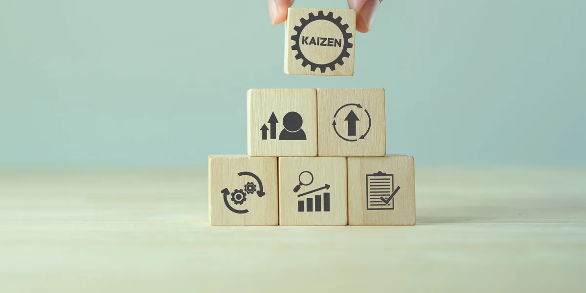Finger heben einen Würfel mit der Aufschrift "Kaizen" von einer Würfelpyramide. © Adobe Stock, Parradee