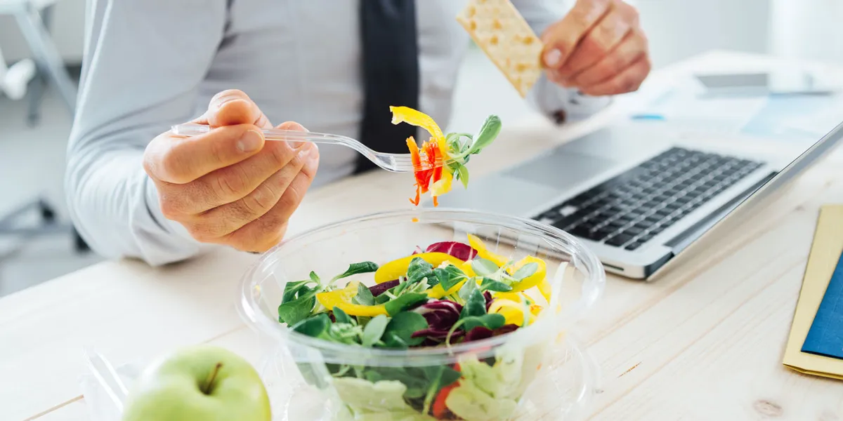 Mitarbeiter achtet auf gesunde Ernährung und isst einen Salat und einen Apfel am Arbeitsplatz. © Shutterstock, Stock-Asso