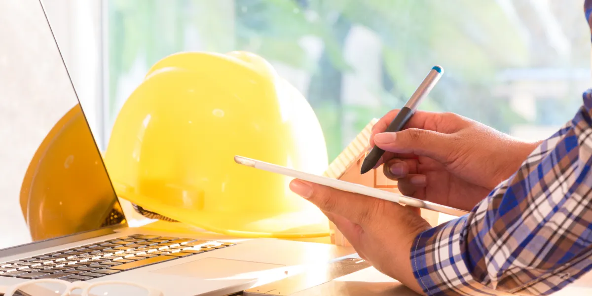 Mitarbeiter arbeitet am Schreibtisch im Homeoffice, neben dem Laptop liegt ein Schutzhelm. © Shutterstock, oekka.k